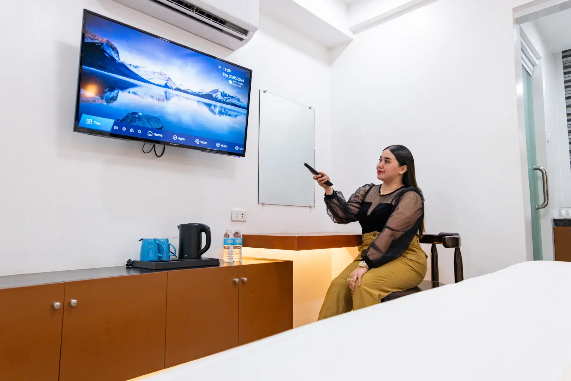 A guest with the TV remote, beside a kettle and bottled water