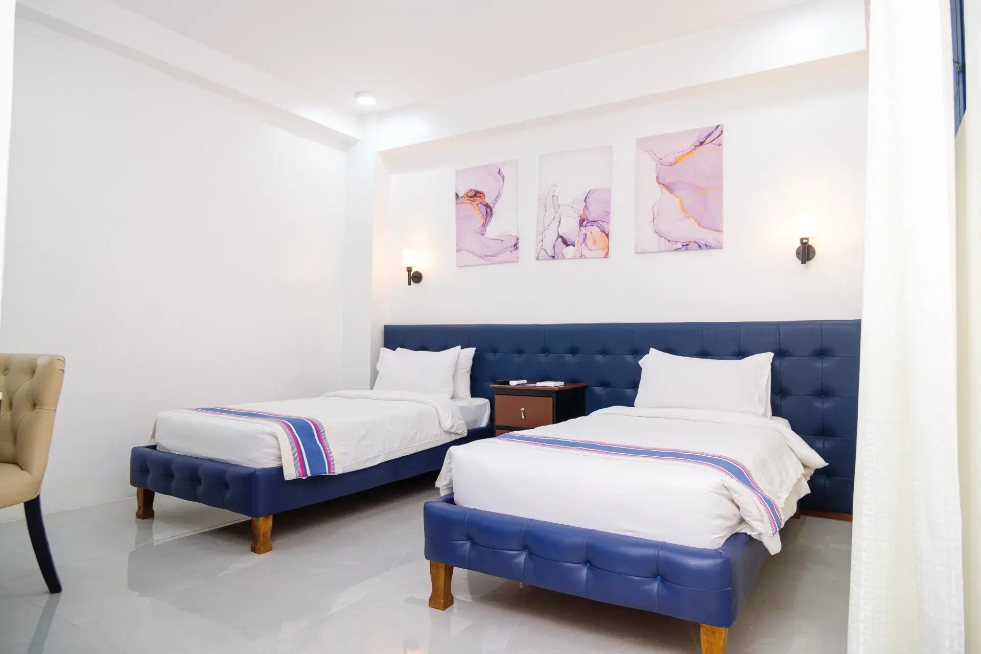 Superior Twin Room: two single beds with navy headboards, under three paintings